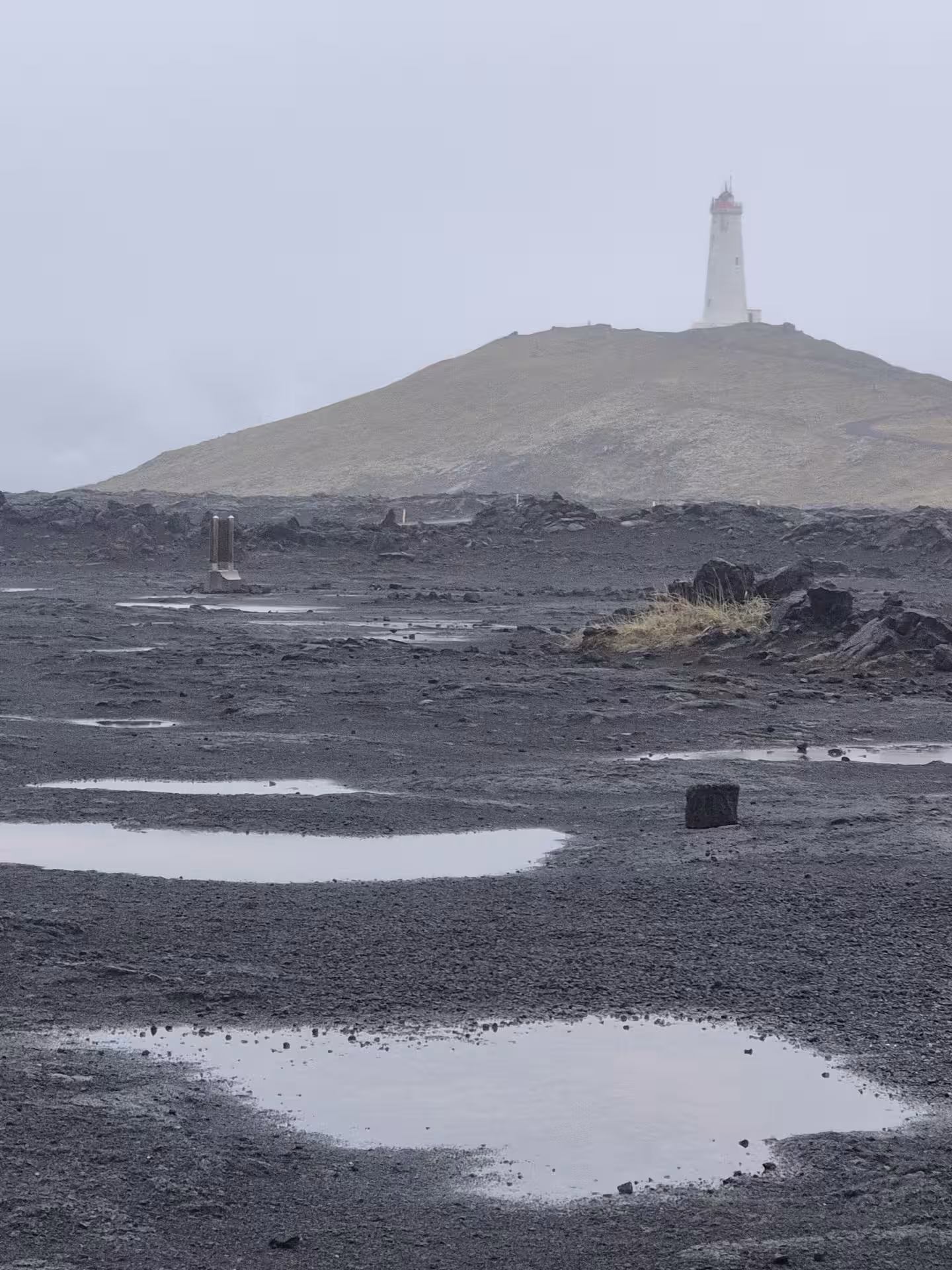 Lighthouse on volcanic lava field hill with rain puddles on Reykjanes Peninsula, Iceland