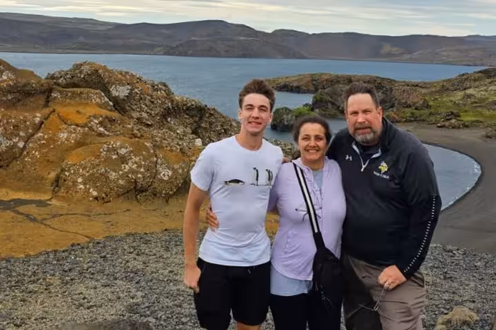 Family of three posing on Reykjanes Peninsula black sand beach with volcanic rocks and lake backdrop