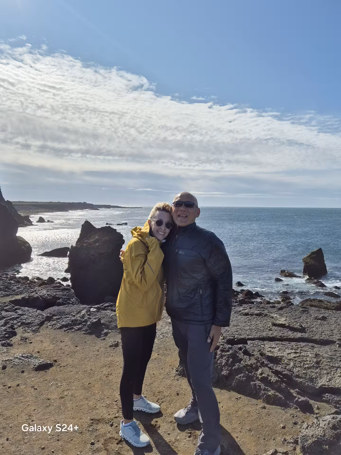 Couple posing on rocky Reykjanes Peninsula coastline with ocean and sea stacks in background