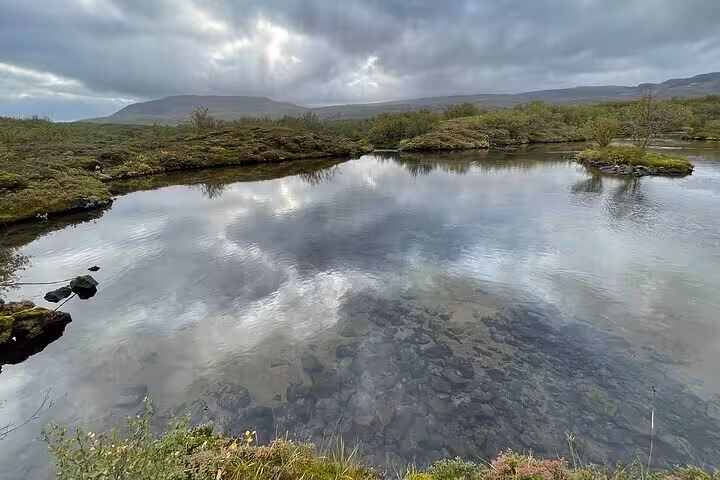 Calm river reflecting cloudy sky surrounded by green mossy tundra and mountains in Iceland