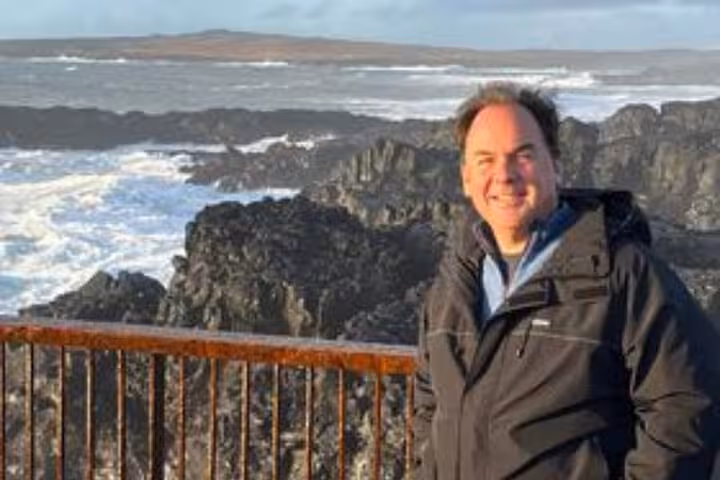 Smiling man in black jacket standing by rocky Reykjanes Peninsula coastline with crashing waves
