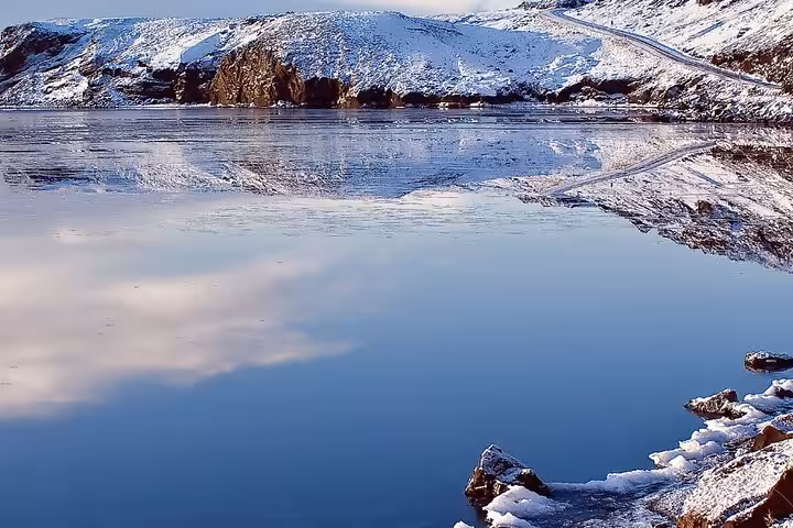 Snow-covered Reykjanes Peninsula hills reflecting in a calm glacial lake during winter tour from Reykjavik