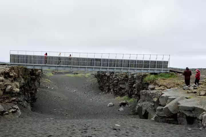 Bridge spanning tectonic plate rift on Reykjanes Peninsula with tourists exploring black lava fields