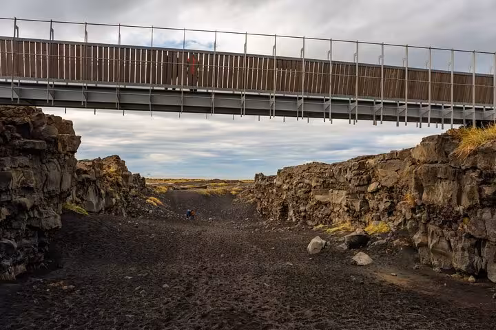 Bridge over tectonic plate rift on Reykjanes Peninsula with black lava rock canyon below