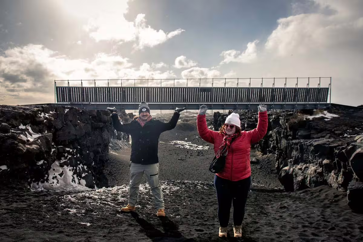 Two tourists posing at the bridge between tectonic plates on Reykjanes Peninsula, Iceland