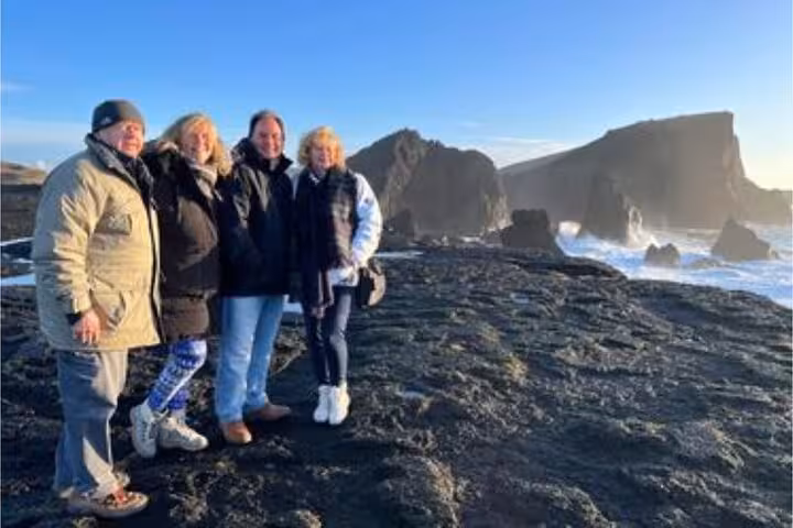 Four tourists posing on volcanic black rock coastline with dramatic sea stacks on Reykjanes Peninsula
