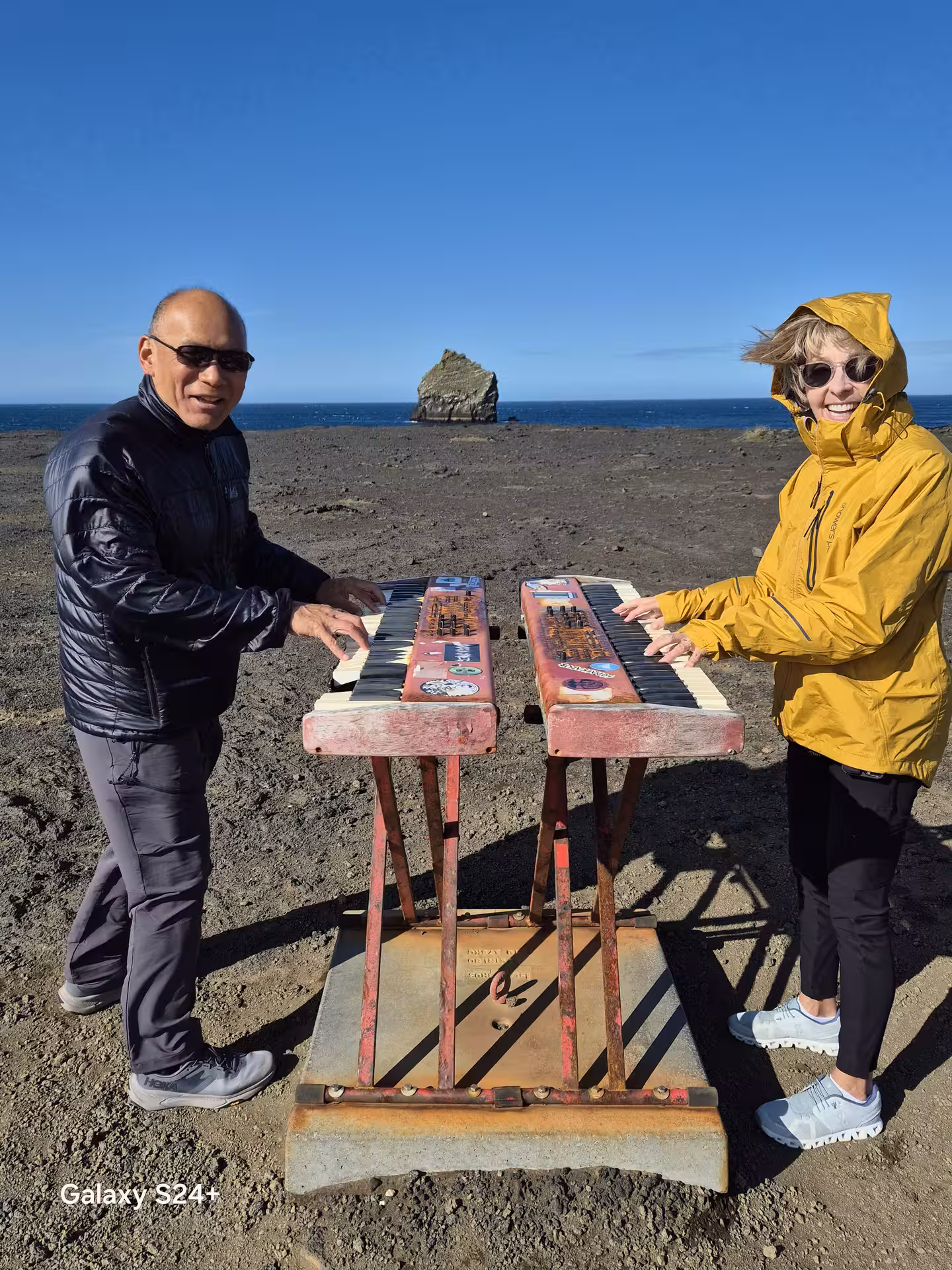 Two tourists playing weathered outdoor keyboards on the volcanic Reykjanes Peninsula coastline, Iceland