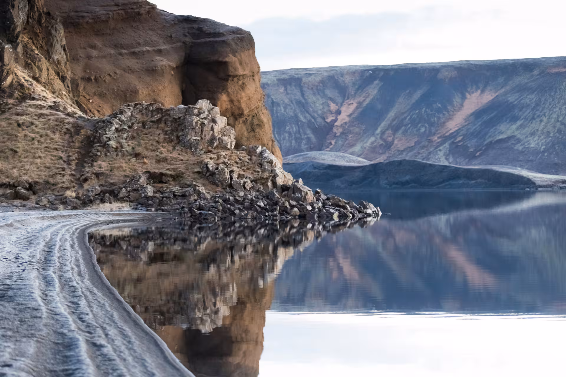 Dramatic volcanic cliffs reflected in calm lake waters on the Reykjanes Peninsula, Iceland
