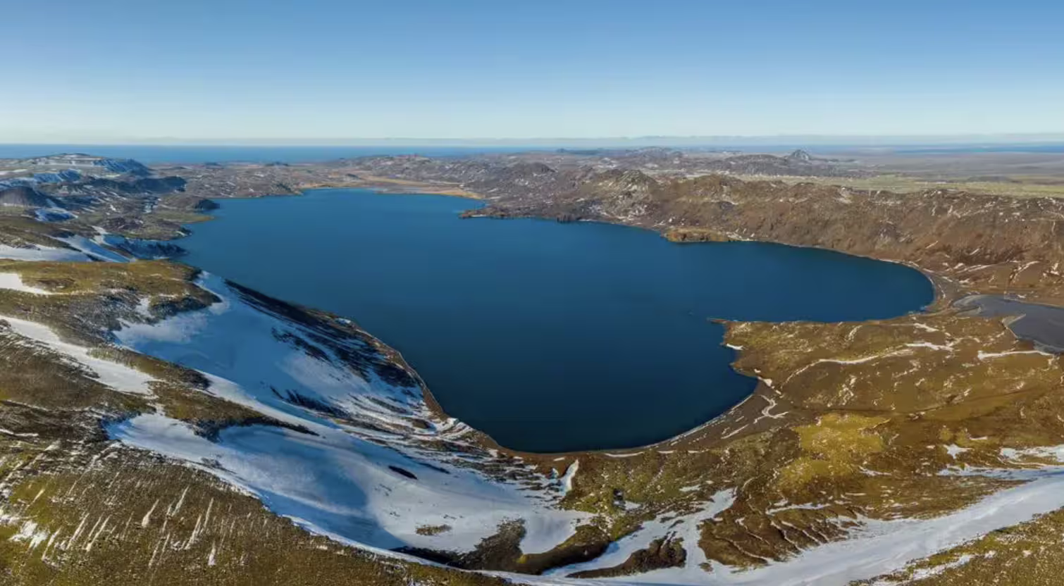 Aerial view of a deep blue volcanic lake surrounded by snow-dusted lava fields on Reykjanes Peninsula, Iceland