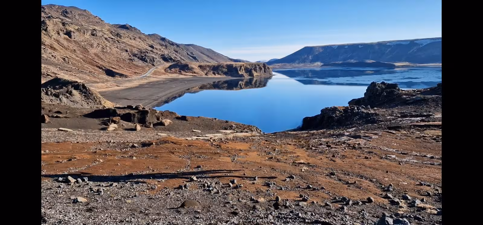 Calm blue volcanic lake surrounded by rugged lava rocks and barren mountains on Reykjanes Peninsula, Iceland