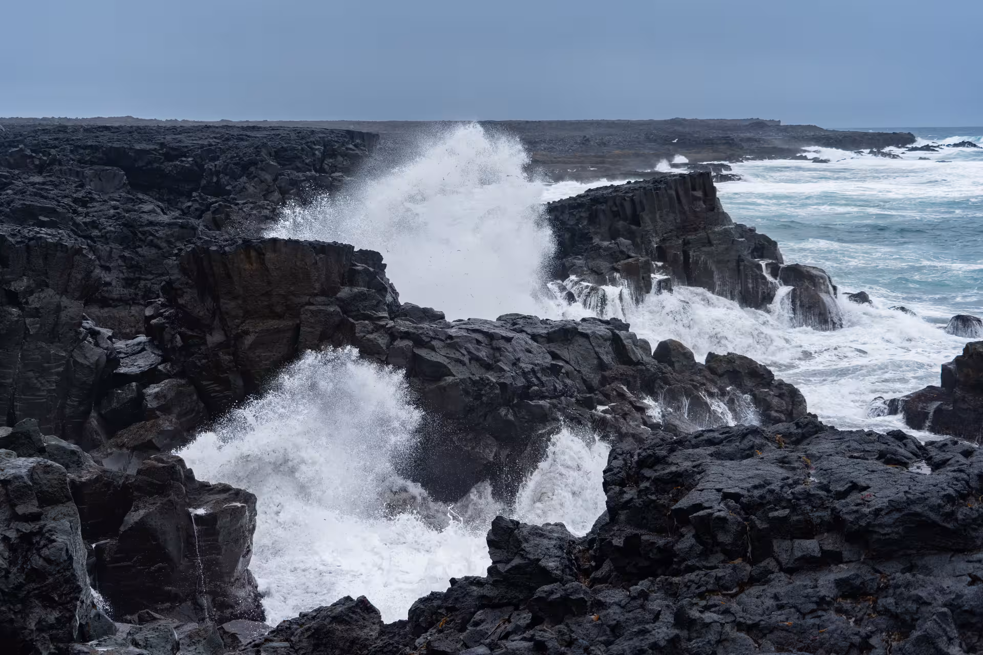 Powerful ocean waves crashing against dark volcanic lava rock cliffs on the Reykjanes Peninsula, Iceland