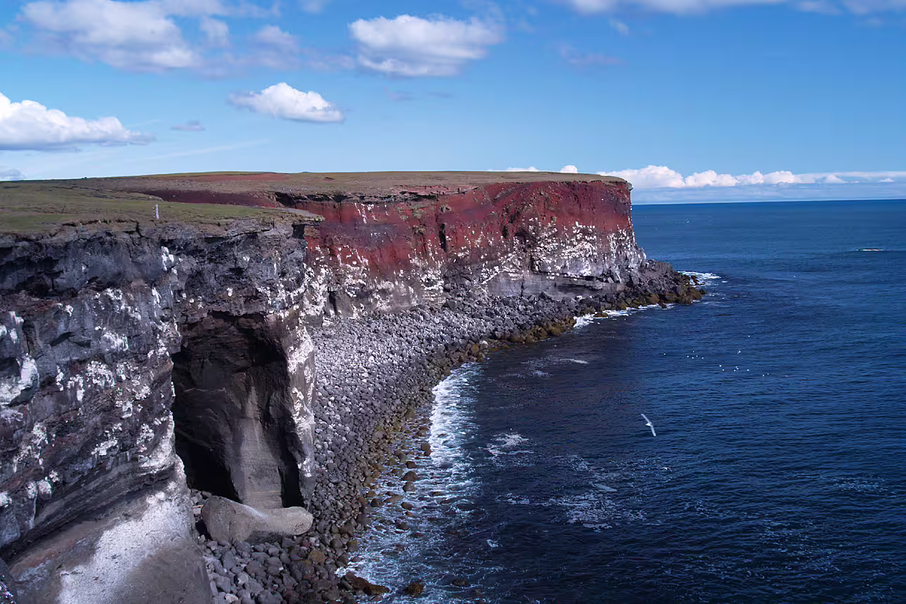 Dramatic volcanic sea cliffs with red and black rock layers along the Reykjanes Peninsula coastline