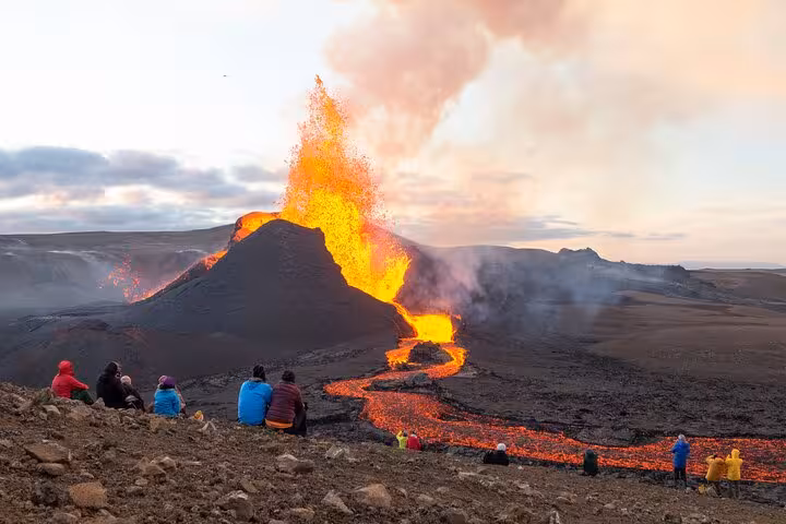 Tourists watching active lava fountain eruption and flowing lava river on Reykjanes Peninsula Iceland volcano hike