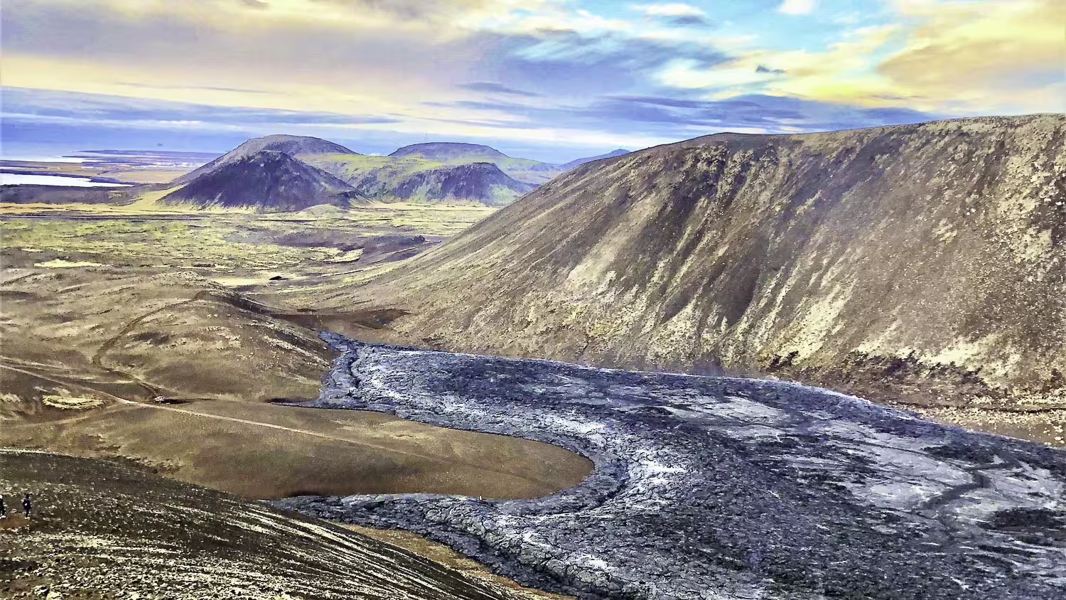 Lava flow winding through volcanic valley on Reykjanes Peninsula with green hills in background