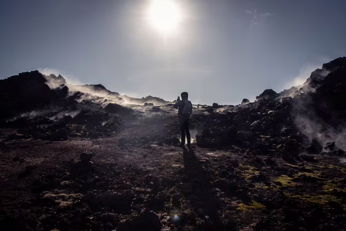 Hiker silhouetted against the sun on steaming volcanic lava fields of the Reykjanes Peninsula