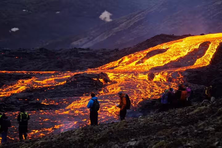 Hikers watching glowing lava flows on Reykjanes Peninsula volcano tour at dusk, Iceland