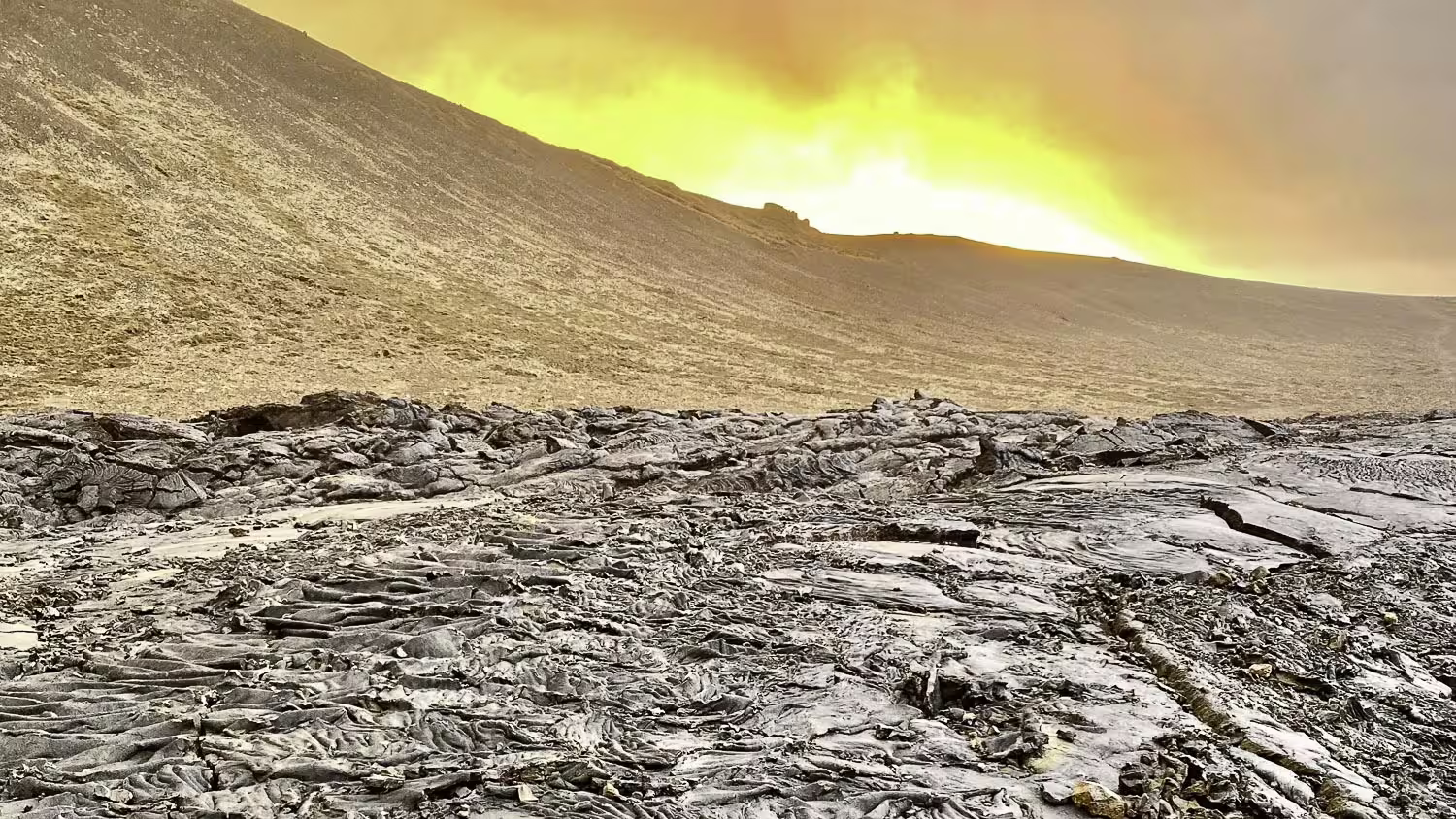 Cooled black lava field on Reykjanes Peninsula with glowing volcanic eruption on horizon