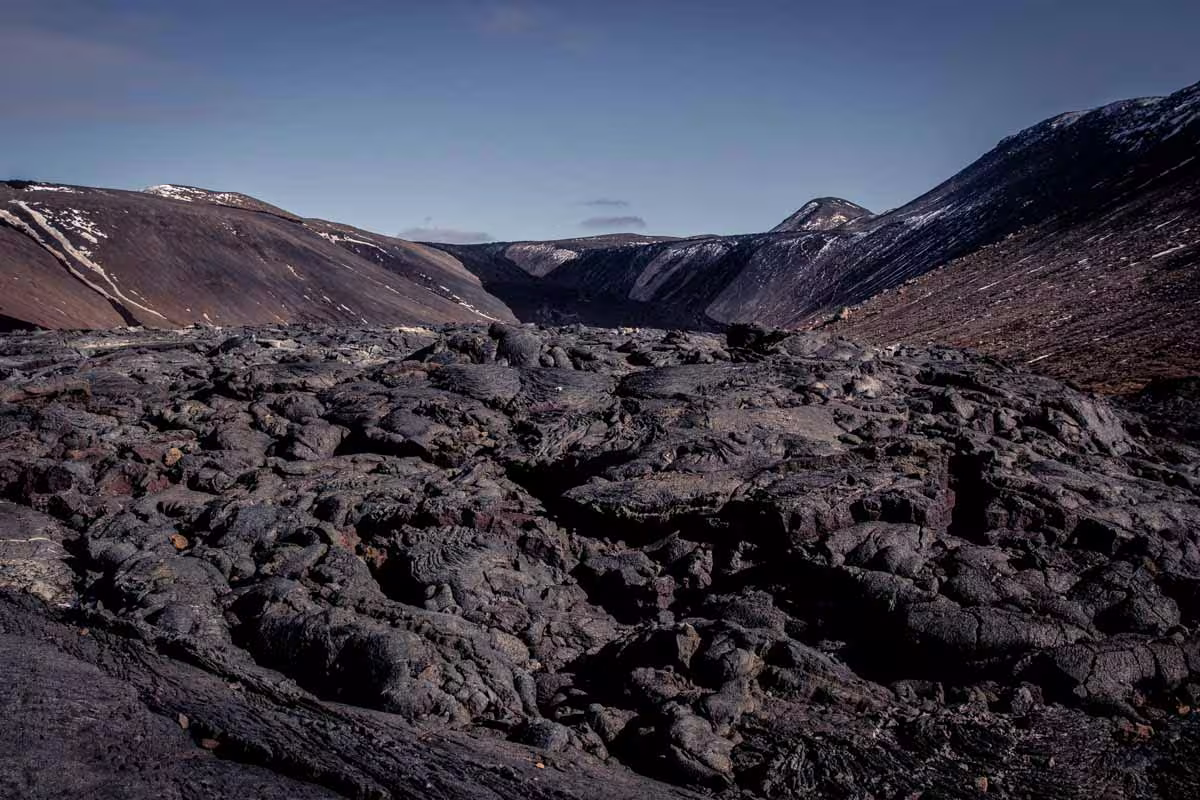 Black hardened lava field with rugged volcanic rock formations and snow-capped mountains on Reykjanes Peninsula