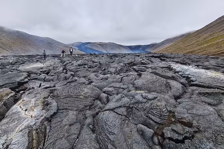Visitors walking on cooled lava field at Reykjanes Peninsula volcano with misty mountains in background