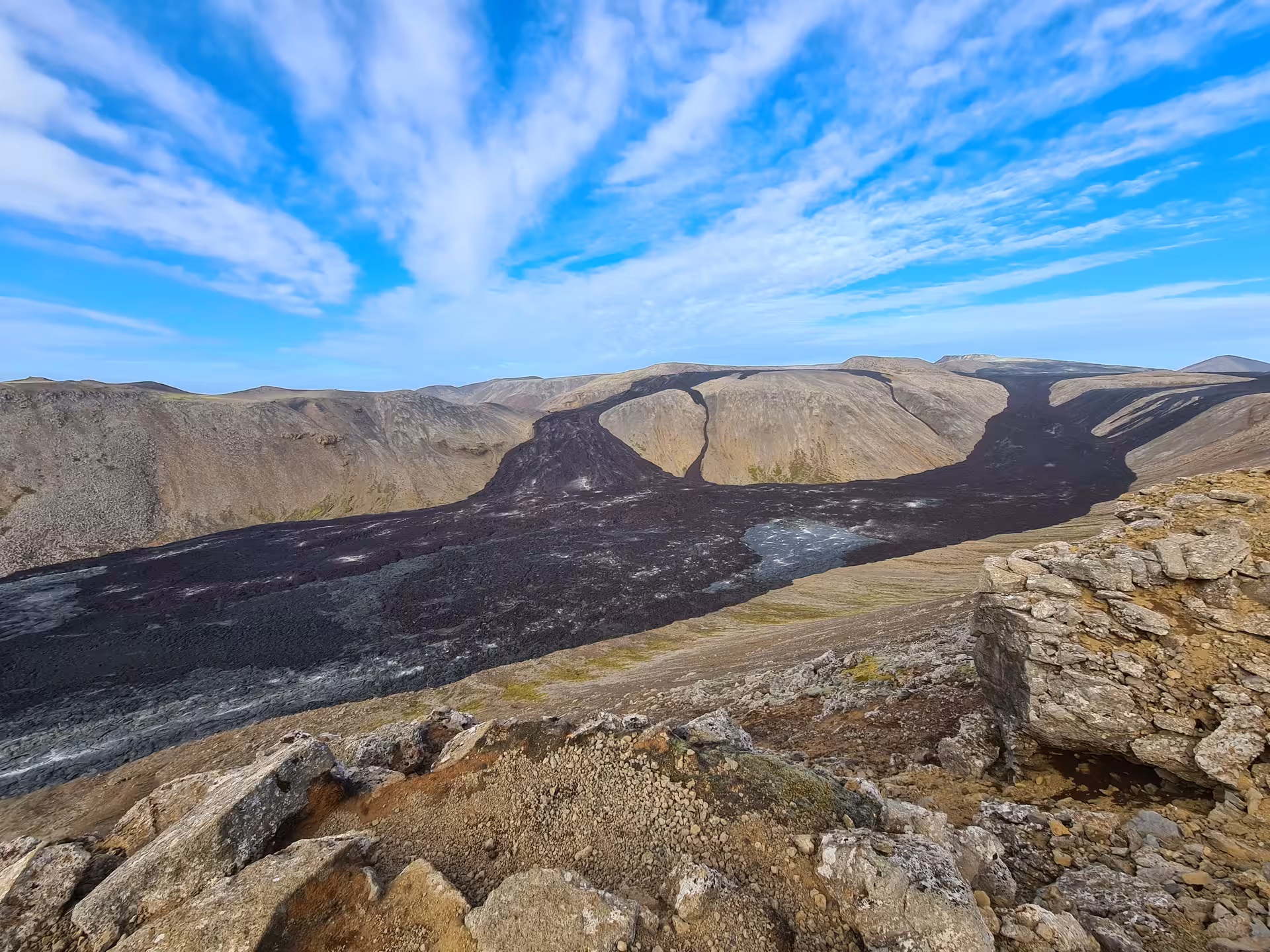 Black lava flow cutting through volcanic highland landscape on Reykjanes Peninsula, Iceland under blue sky