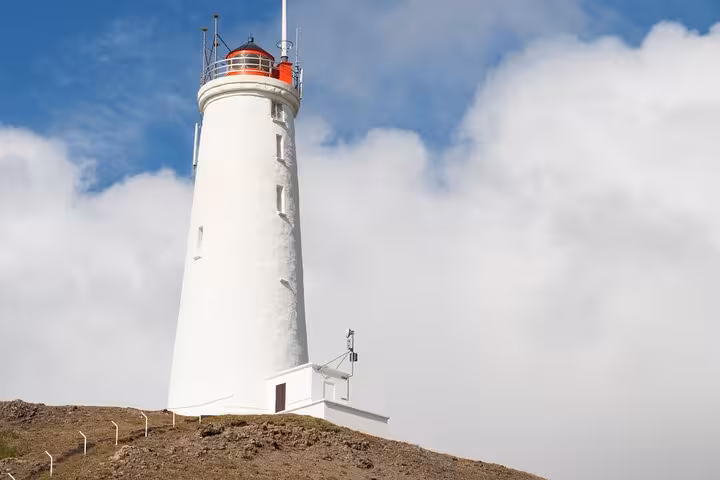 White lighthouse with red lantern room on rocky hilltop under blue sky on Reykjanes Peninsula