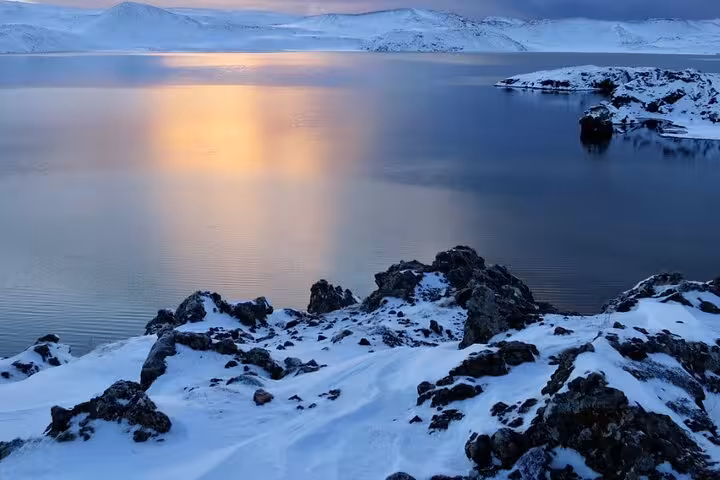Snowy volcanic rocks along calm fjord at sunset on Reykjanes Peninsula, Iceland