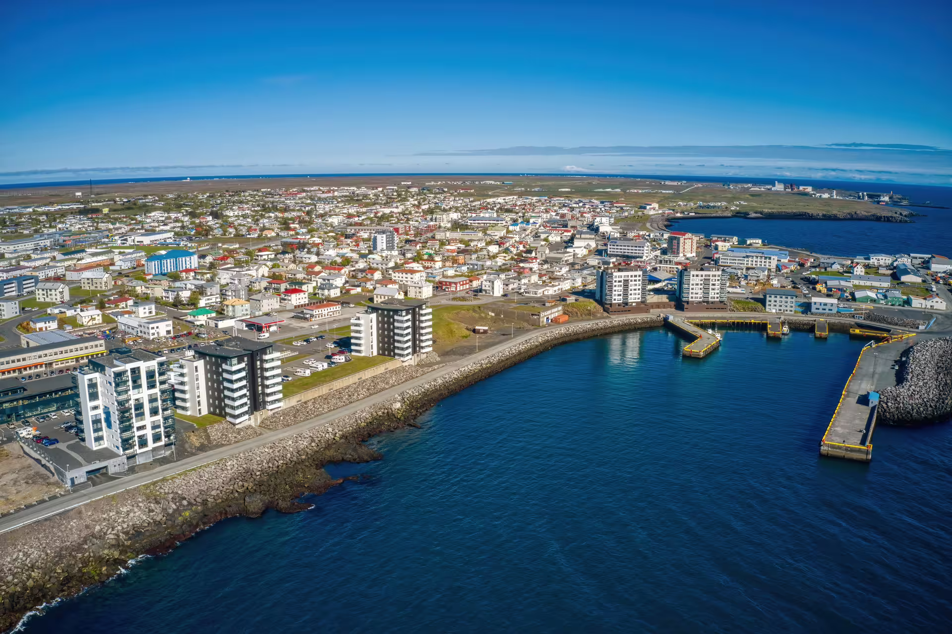 Aerial view of Reykjanes town coastline with harbor, colorful buildings, and blue ocean waters on a sunny day