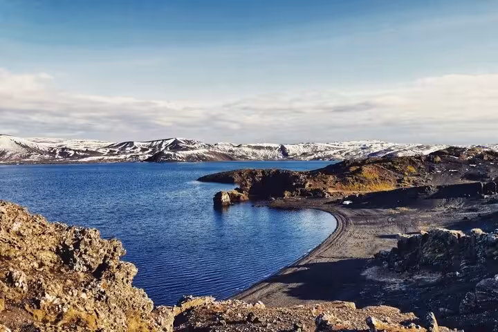 Blue volcanic lake with black lava shores and snow-capped mountains in Reykjanes Peninsula, Iceland
