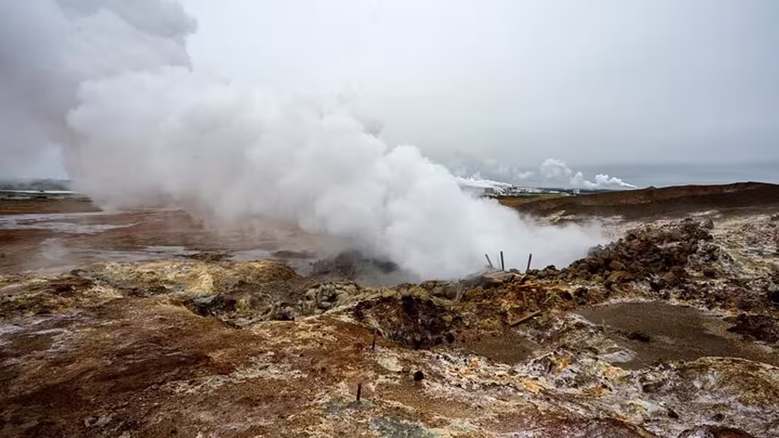 A volcanic landscape with large clouds of steam vising from a vent