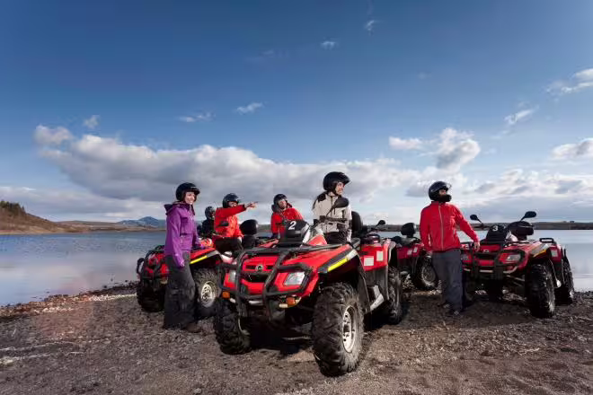 Group of riders on red ATVs parked by a lake shore in Iceland under blue sky