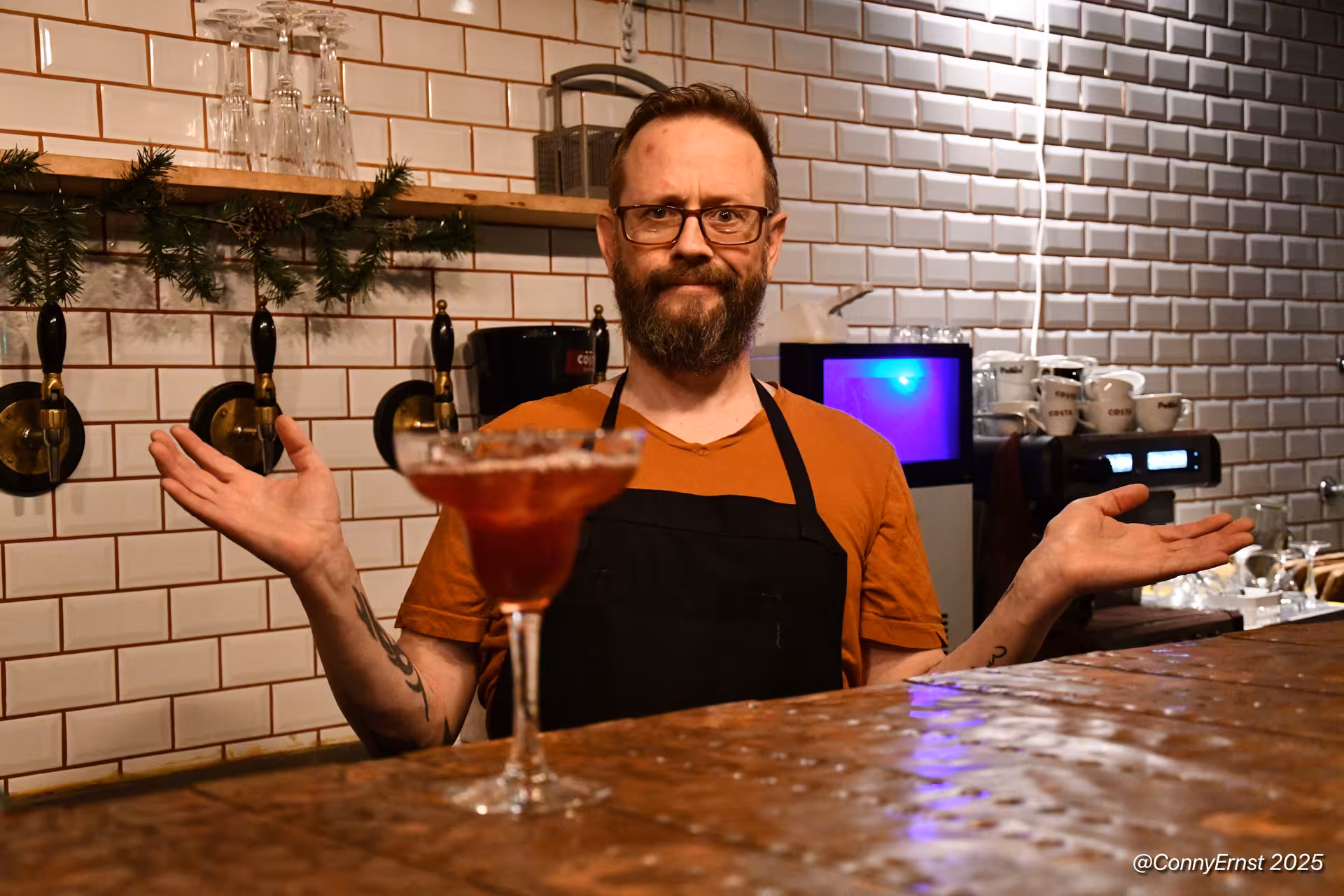 Bearded bartender in black apron presenting a red cocktail at a bar in Reykjavik, Iceland