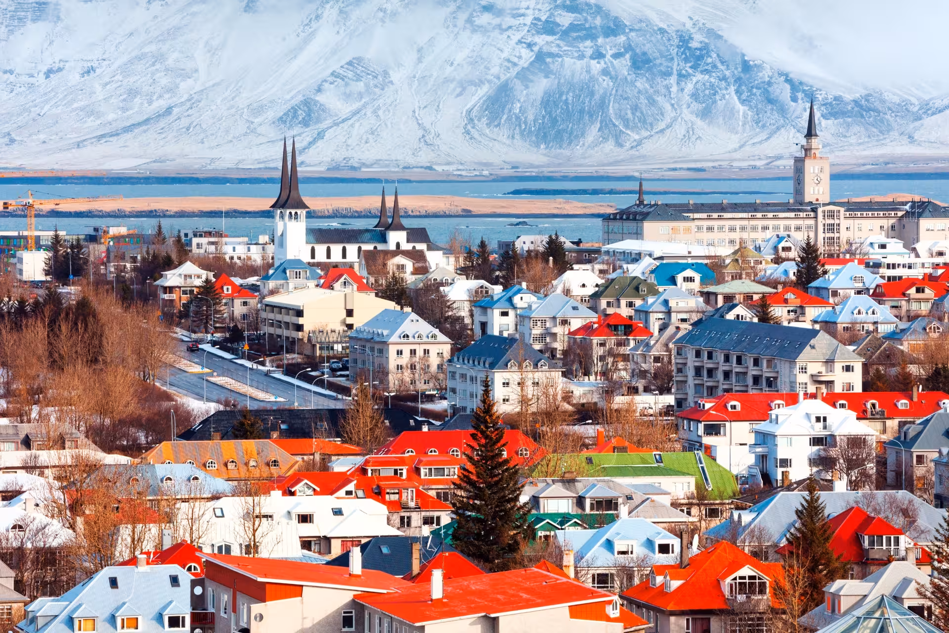 Aerial view of colorful rooftops in Reykjavik city with snow-capped mountain backdrop in winter