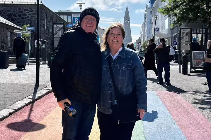 Couple smiling on rainbow crosswalk in Reykjavik city center with Hallgrímskirkja church in background