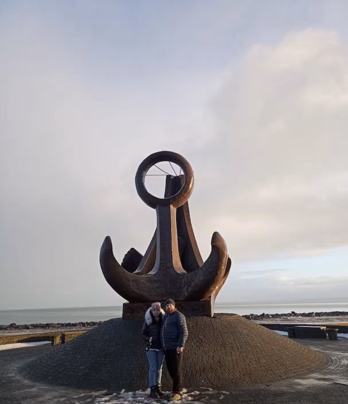 Couple posing in front of large anchor monument near Reykjavik cruise port in winter