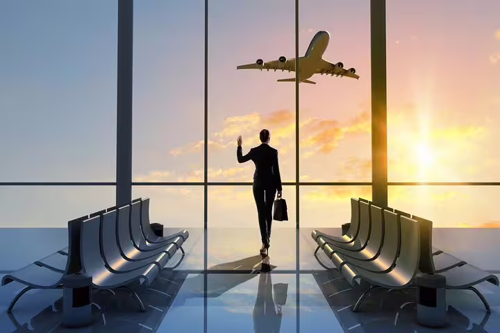 Business traveler waving goodbye at airport terminal with airplane flying at sunset