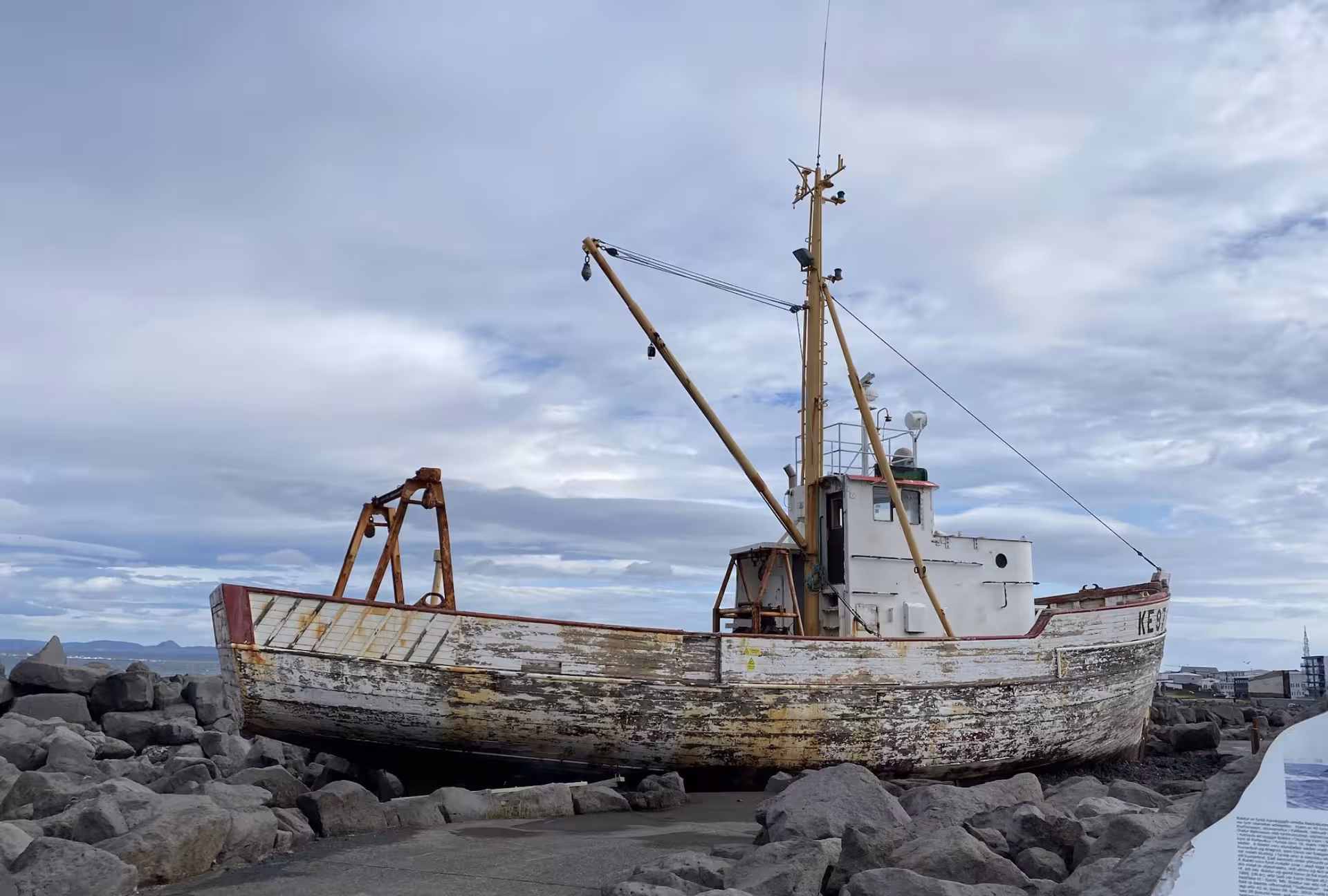 Weathered wooden fishing boat displayed on rocky shore at Reykjavik cruise port