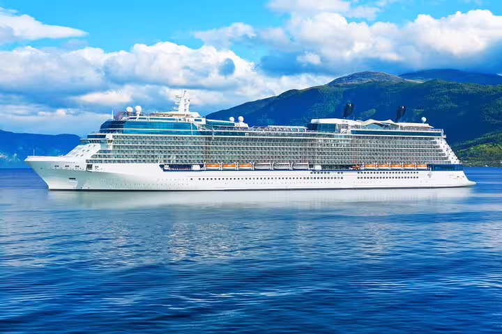 Large white cruise ship sailing on calm blue waters with green mountains in background