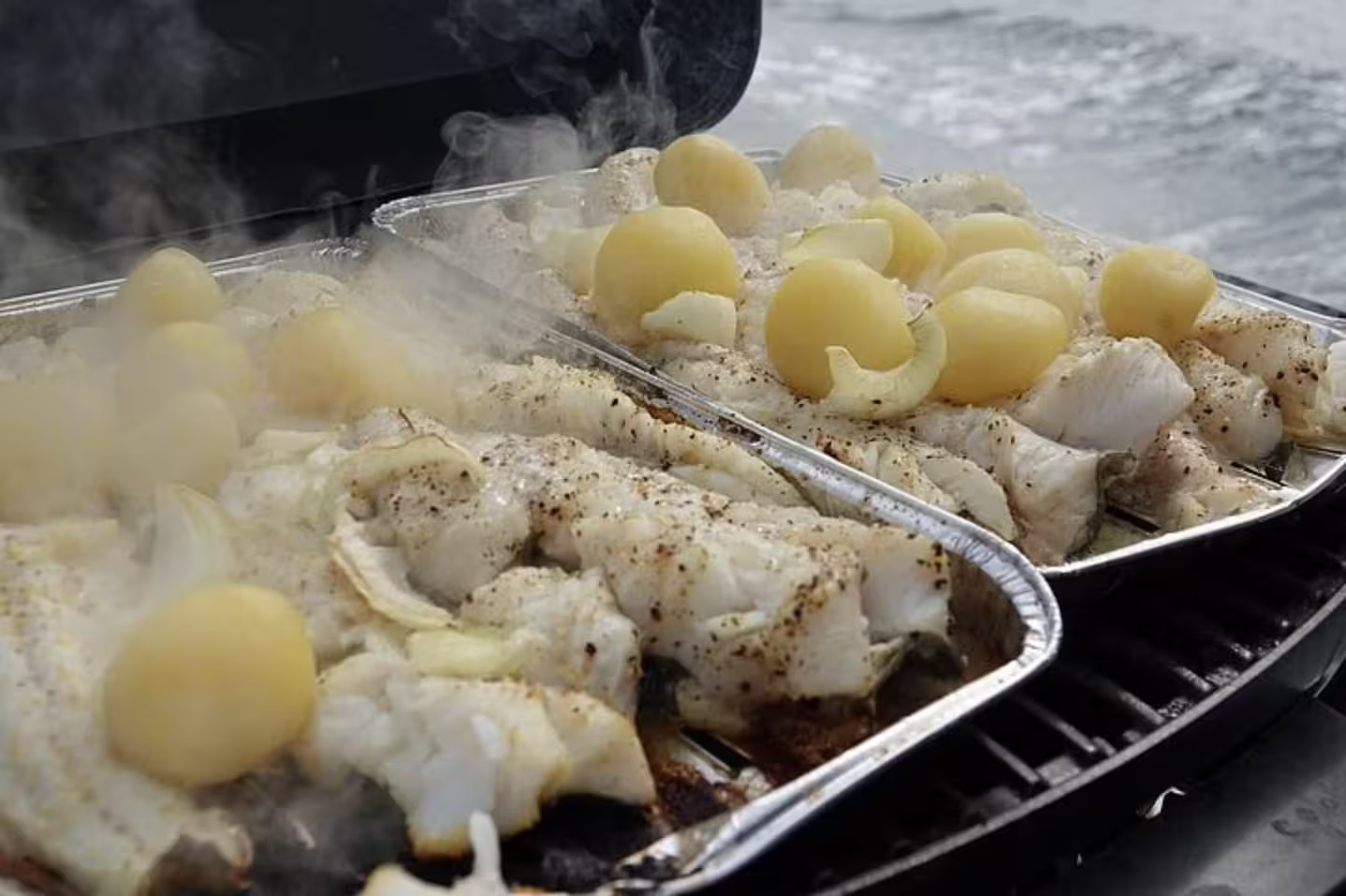 Steaming grilled fish fillets and boiled potatoes cooking in foil trays on a Reykjavik fishing boat