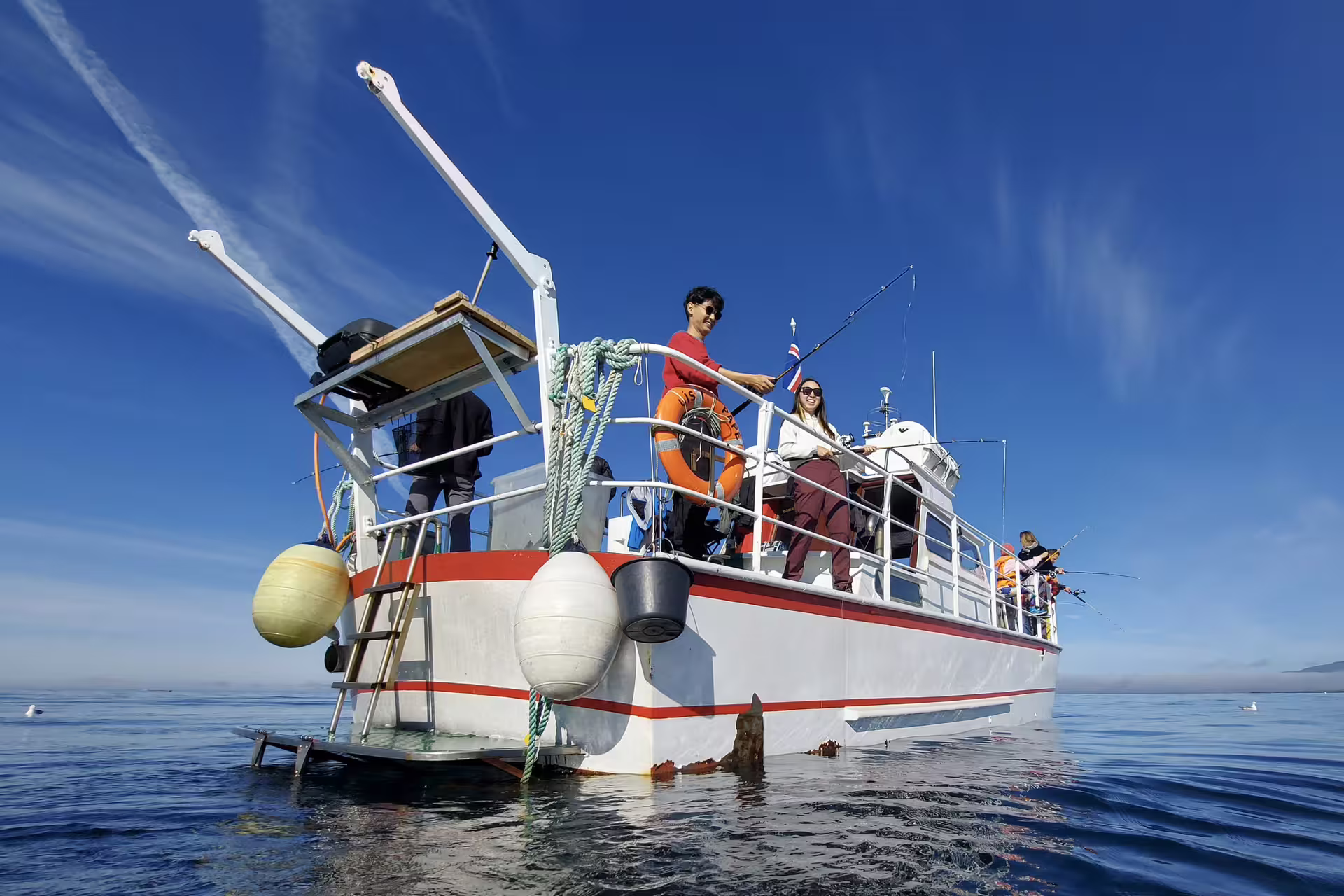Tourists fishing from a white boat on calm blue waters in Reykjavik on a sunny day