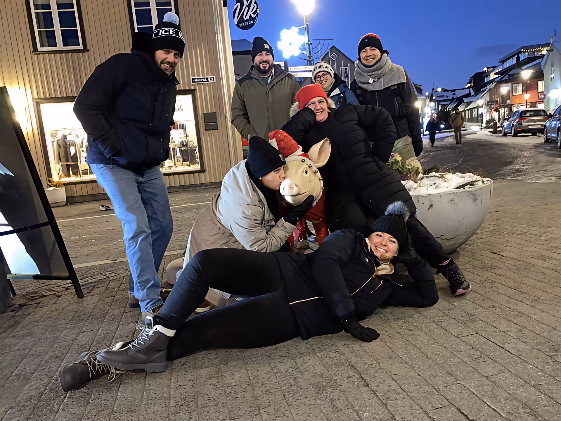 Group of tourists laughing with a pig statue on a snowy Reykjavik street at night