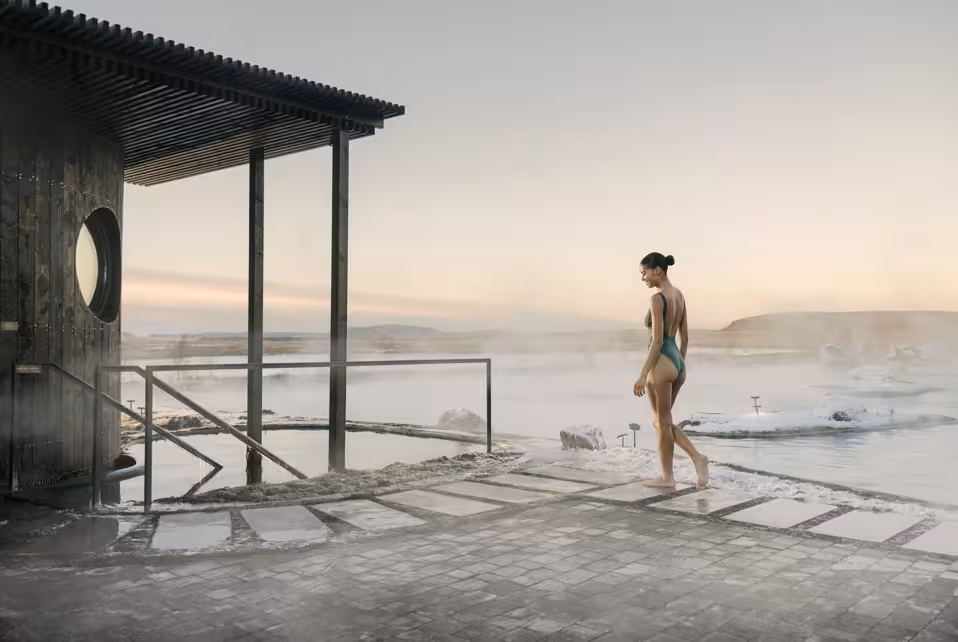 Woman in swimsuit walking along steaming geothermal hot spring pool in Iceland winter landscape