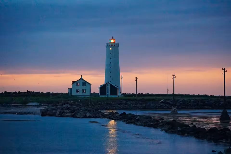 Reykjavik private city tour featuring Grotta lighthouse glowing at sunset over calm coastal waters in Iceland