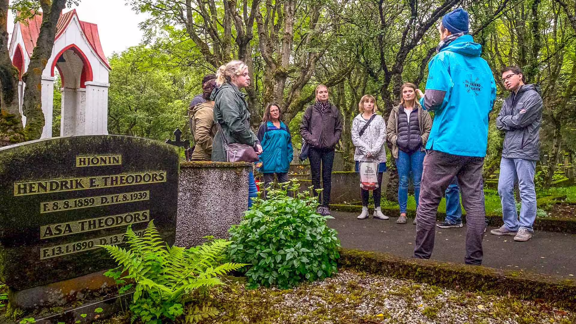 Tour guide leading a group at a historic gravestone in a lush Reykjavik cemetery