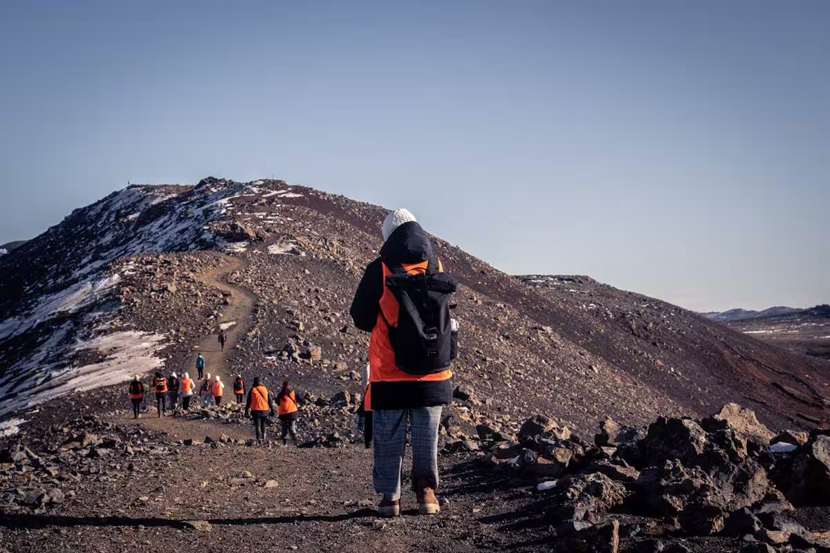 Guided group hiking up rocky volcanic trail on Reykjanes Peninsula with orange vests and snowy terrain