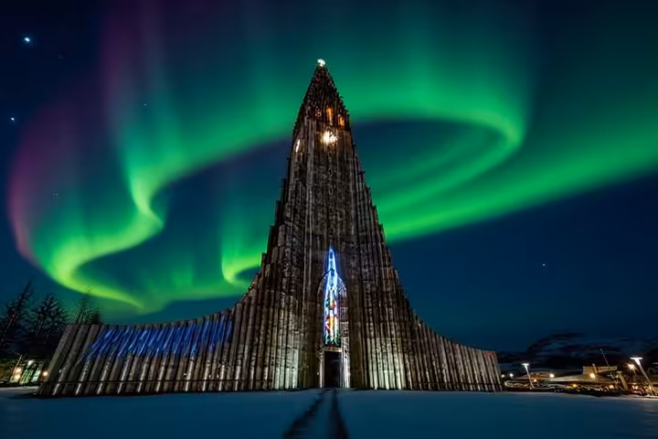 Hallgrímskirkja church in Reykjavik illuminated at night with vibrant green aurora borealis swirling overhead in winter