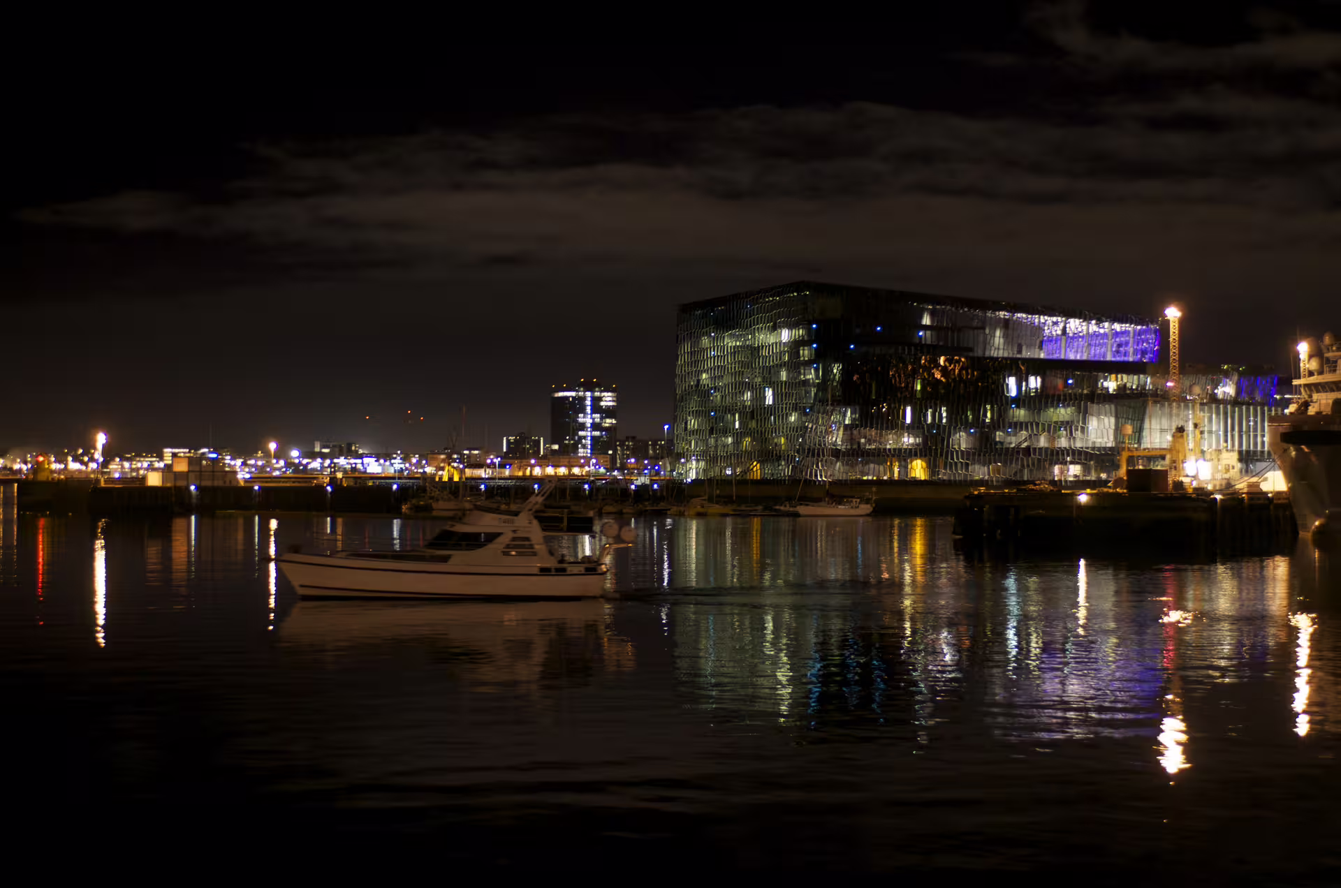 Harpa Concert Hall illuminated at night reflected in Reykjavik harbor with moored boat in foreground