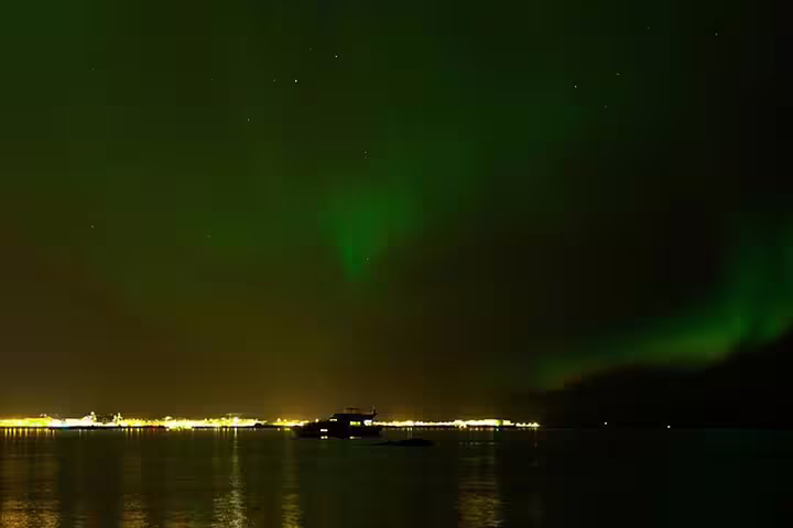 Aurora borealis glowing green over Reykjavik harbor at night with city lights reflecting on water