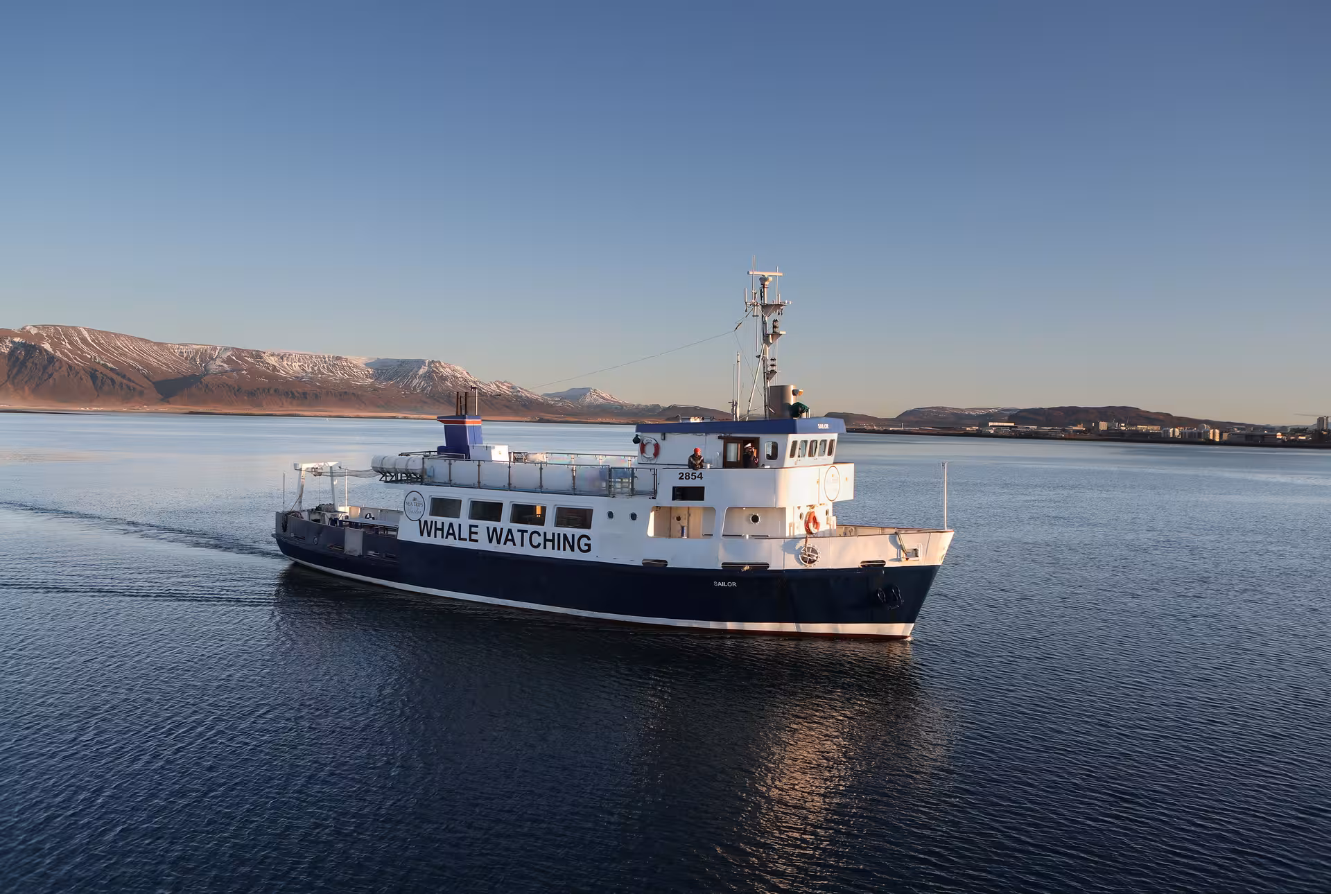 Whale watching boat sailing calm waters near Reykjavik with snow-capped mountains in background