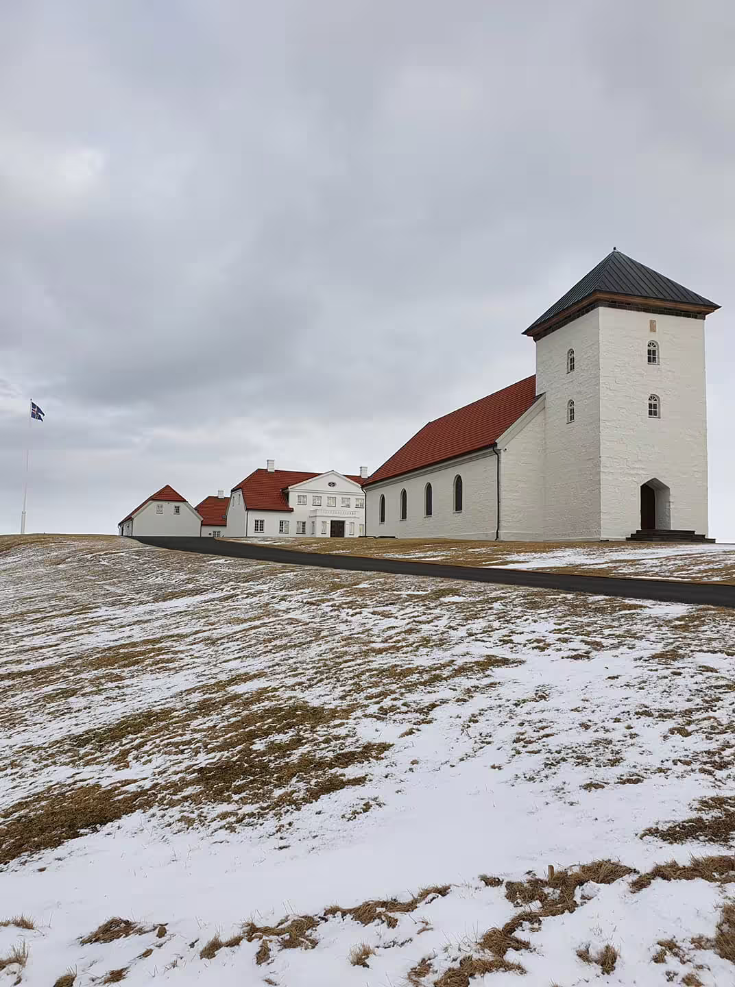 White church with tower and red roofs on snowy hill in Reykjavik with Icelandic flag