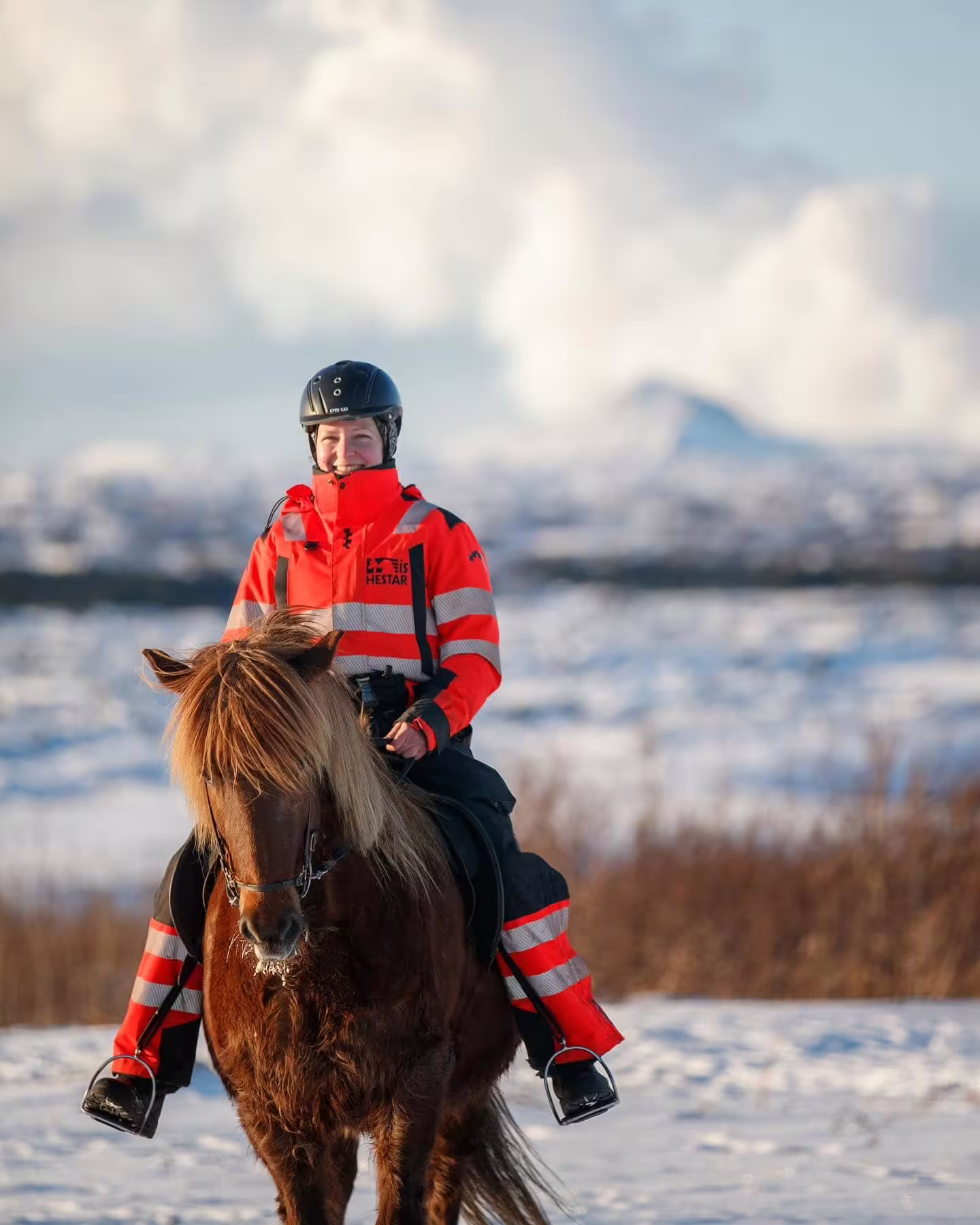 Smiling rider in red jacket on Icelandic horse in snowy winter landscape